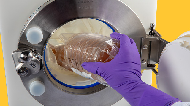 A close-up image of a gloved hand placing a sealed petri dish into a circular opening of a laboratory device. The device features a metal rim and a bright blue background, emphasizing a sterile and controlled environment for scientific work.