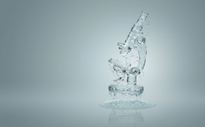 A transparent glass microscope with water droplets suspended in mid-air, set against a light gray background