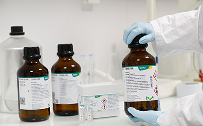 Cover picture representing a webinar on 'Karl Fischer Titration Series' showcasing three brown colored reagent bottles, with one transparent bigger bottle at their back and gloved hands of a lab chemist wearing a lab coat opening ampoules with two ampoules kept outside their box.
