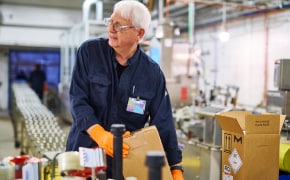 A photo featuring an operator packing products in a factory next to a production line.