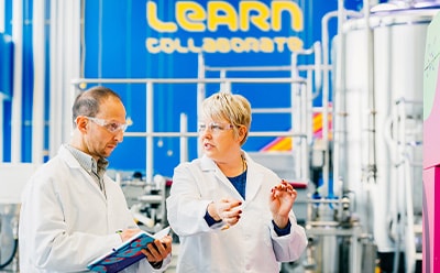 This image shows two scientists in the MLab with bioreactors in the background.