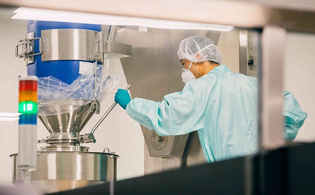 Technician overseeing bioreactor for chemical processing, featuring a professional in protective clothing meticulously monitoring a stainless steel bioreactor, which is integral to downstream processing and formulation in the chemical industry, within a cleanroom environment.