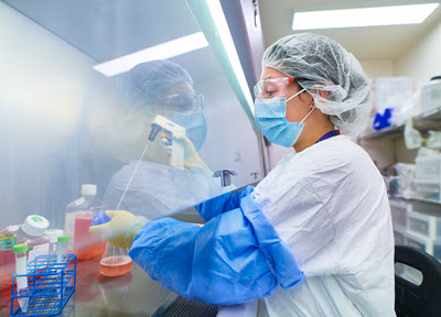 Researcher wearing safety gear in a laboratory working with a substance behind a protective barrierwearing a lab coat, gloves, facemask, protective glasses working with a substance behind a protective shield. 