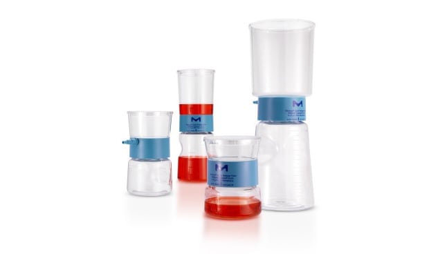 Stericup® Quick Release filters for sterile filtration category page A collection of five laboratory volumetric tools with varying amounts of liquid. From left to right, there is a small beaker with red liquid reaching the measurement line, a graduated cylinder half-filled with red liquid, another graduated cylinder with a smaller amount of liquid at the bottom, an empty volumetric flask on top of an upside-down beaker, and finally, a large beaker half-filled with clear liquid. The tools are marked with measurement lines and are placed against a white background.