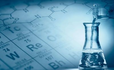 实验室场景中，一只装满液体的透明玻璃烧瓶静静矗立，上方悬着一只滴管。背景中隐约可见元素周期表，整个画面笼罩在蓝调氛围中，营造出科学研究环境的氛围。