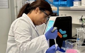 Aditi wears PPE and uses a pipette to extract a solution in the lab.