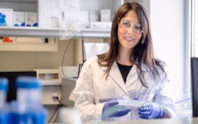 Eleni Samaridou stands in the lab wearing a lab coat, gloves and glasses.