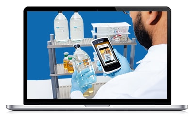 一个身穿白大褂的人拿着智能手机，在蓝色背景下观察一辆装有各种实验室瓶子的推车。