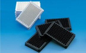 Two piles of 96 well plates, one stacked in the background with one plate slanted and leaning in front, and one group of four plates in a pile on top of each other.