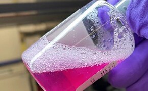 The product bottle of the rehydrated EDM gel, slanted and facing the top right corner. Fingers hold the bottle top.