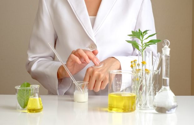 Scientist in a lab coat rubs white cream on the back of their hand with one finger.