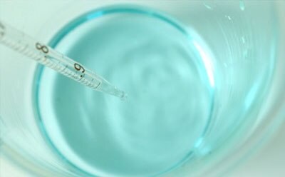 Image of light blue biological buffer solution in beaker with pipette.