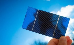 A thin, blue solar cell is held up by hand to sunlight.
