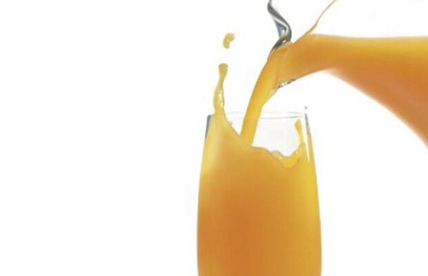 Drinking glass with orange juice being poured and splashing over the top.